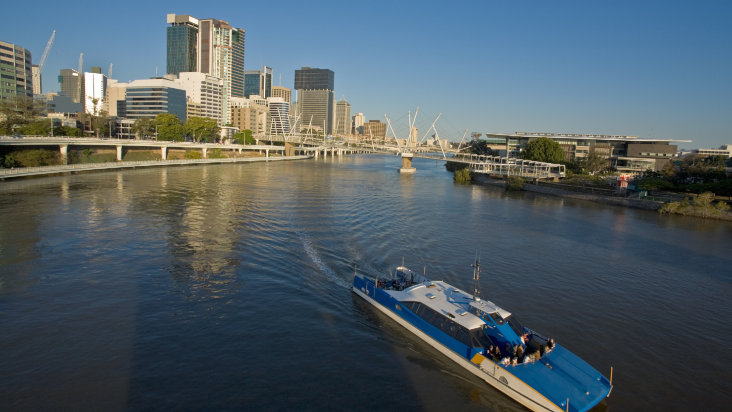 Brisbane's CityCat boat on the Brisbane river with the city skyline behind it.