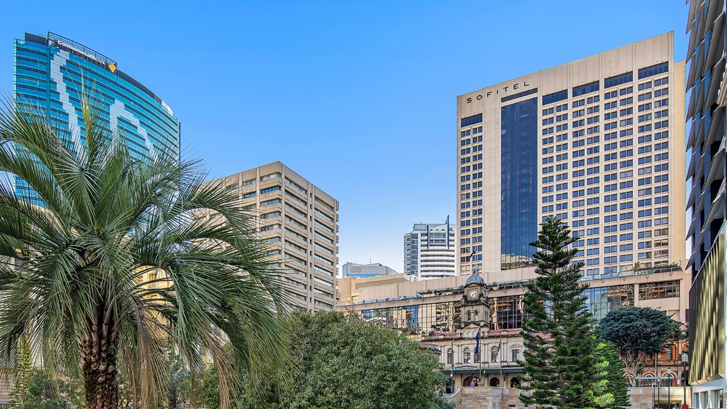 Sofitel Brisbane Central hotel amongst Brisbane's central station with a palm tree and several tall trees in front.